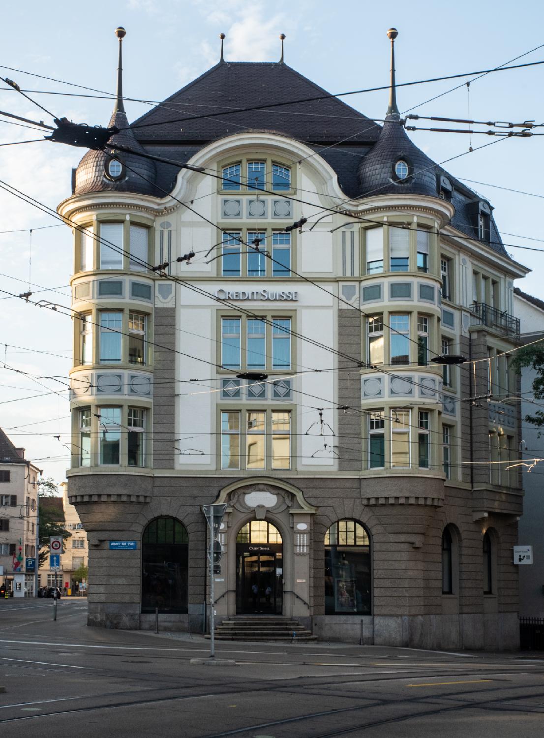 Facade a Credit Suisse building on Albert-Näf-Platz. The sides have bay windows over the height of the building, topped with small domes. The building is criss-crossed by the tram cables that are in front of it.