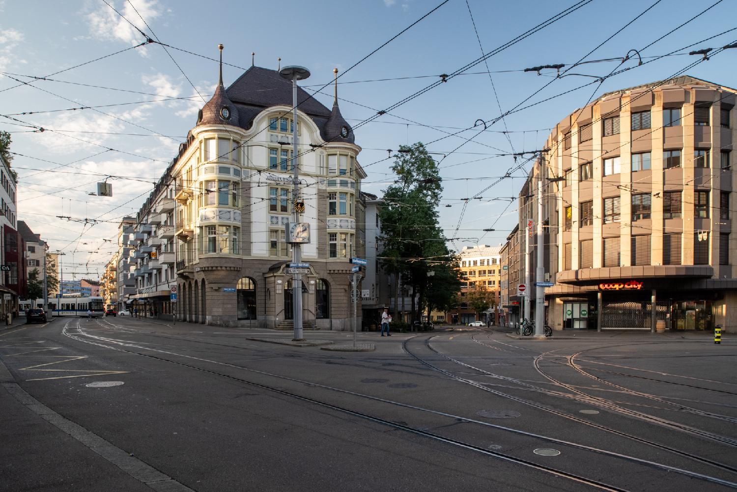 A public square with a few few-stories buildings and tram rails in the foreground.