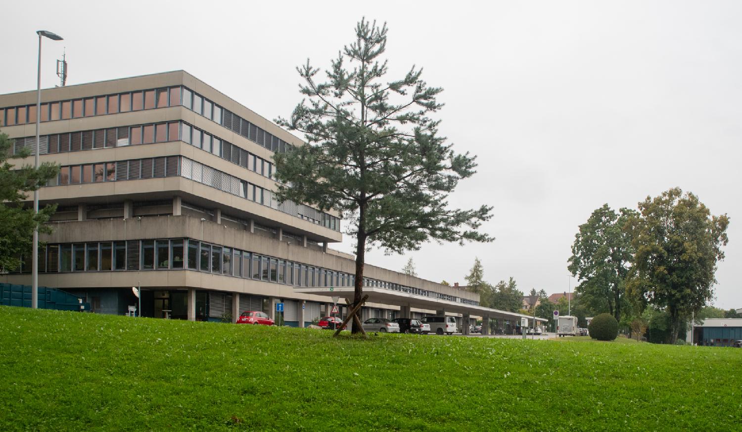 A grey administrative building with a small roofed area with cars waiting for inspection.