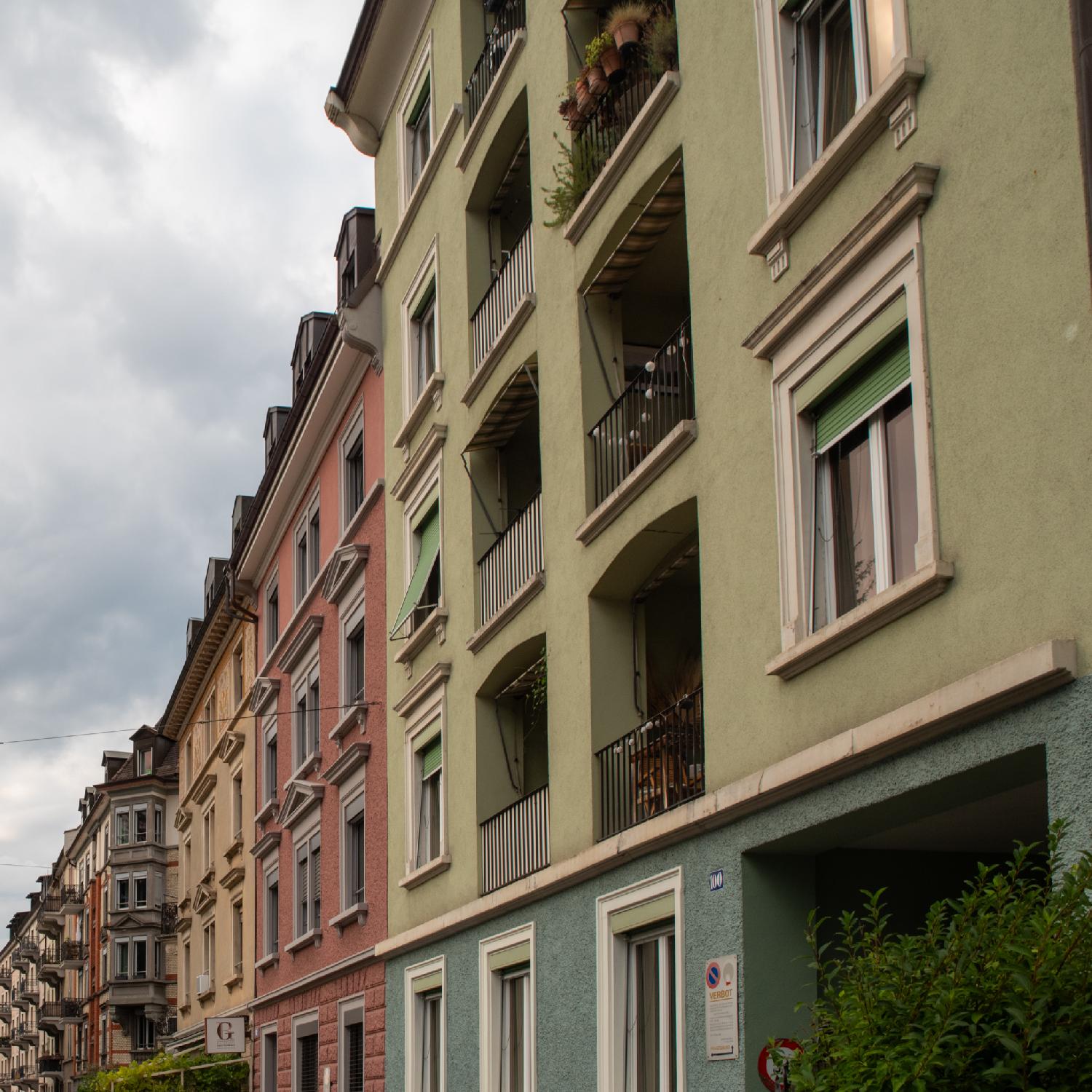 A series of facades in various colors: army green, raspberry, peach , and a grey bay window behind it.