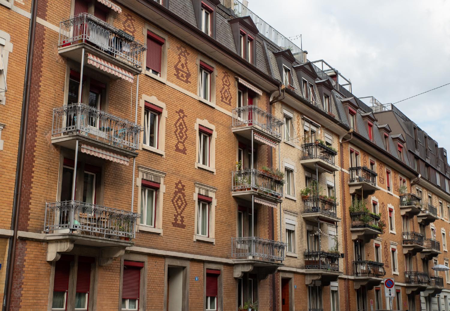 5-storey buildings in various shades of browns with metallic balconies, tiled roofs and dormer windows.