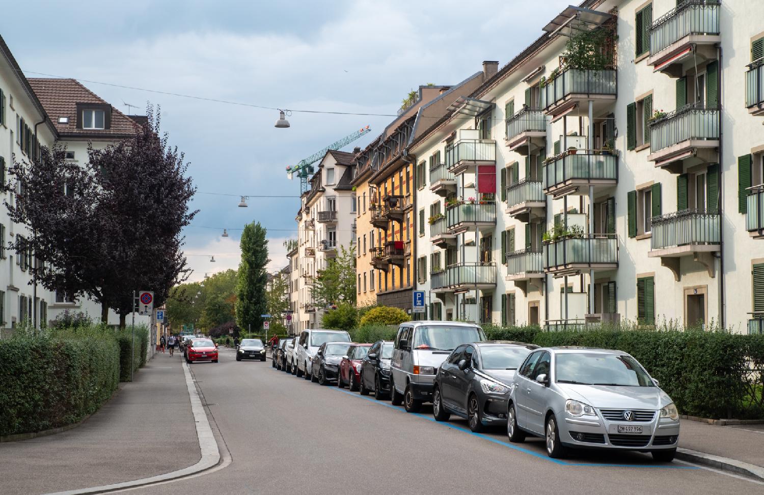 A residential street with 5-storey buildings and cars parked in the street.