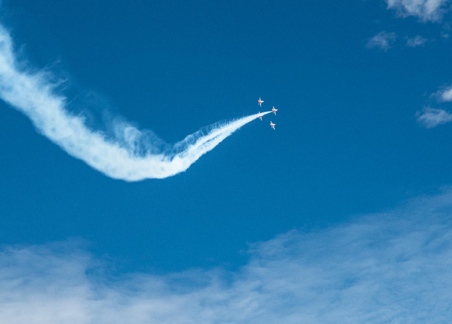 Four jet airplanes flying in formation, with a large curve of white trails behind the lead plane.