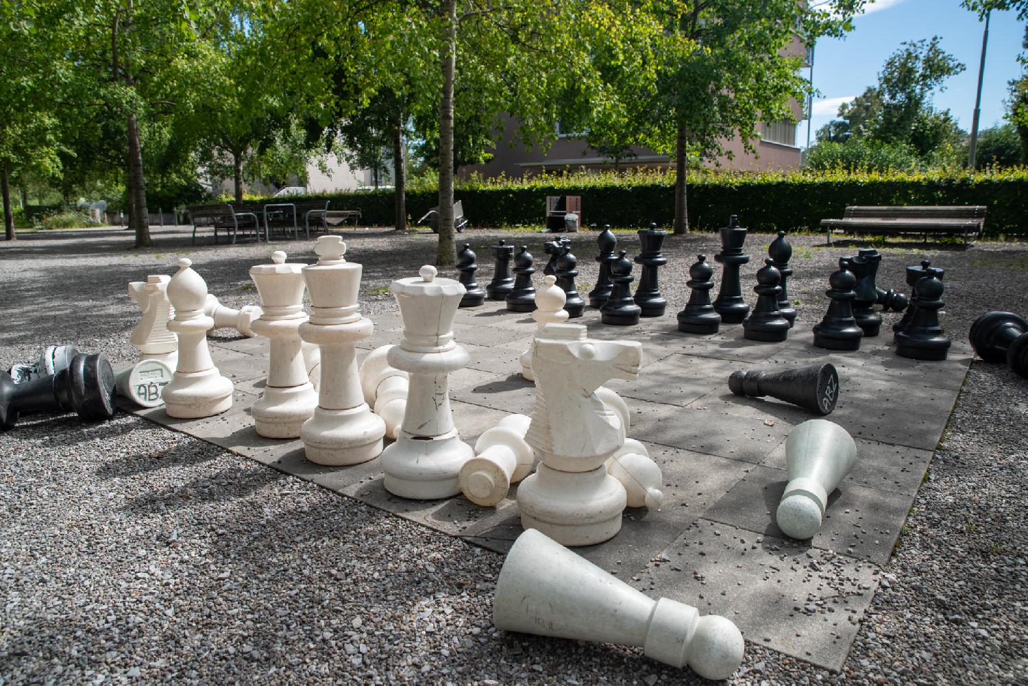 A giant chess set in a park. The pieces are mostly on the board, but some of them have fallen.