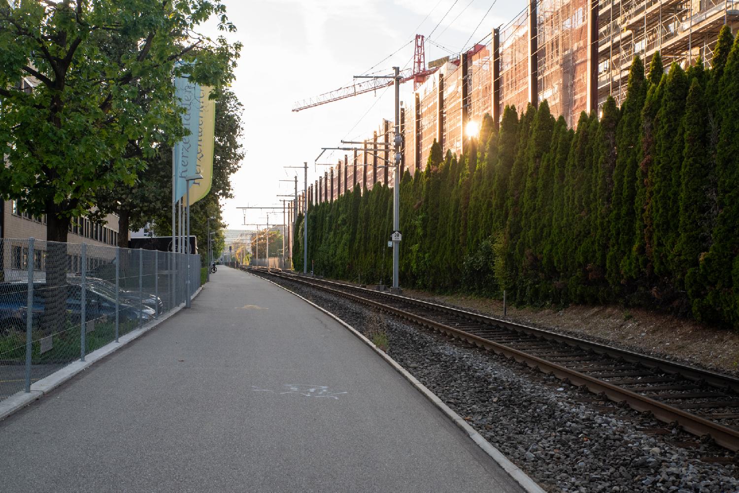 A pedestrian path and a railroad track, side by side with no barrier between them. On the right of the track, there's a high orange palisade with some trees in front of it.