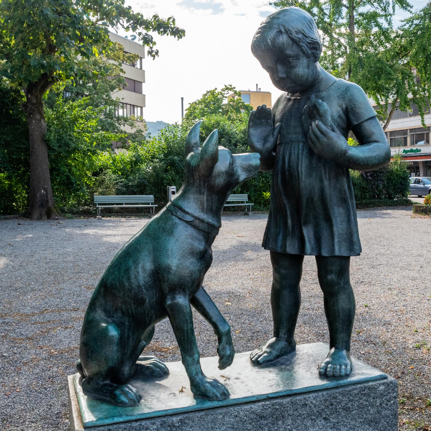 A bronze statue of a child denying the sitting dog in front of them the cookie they have in hand.