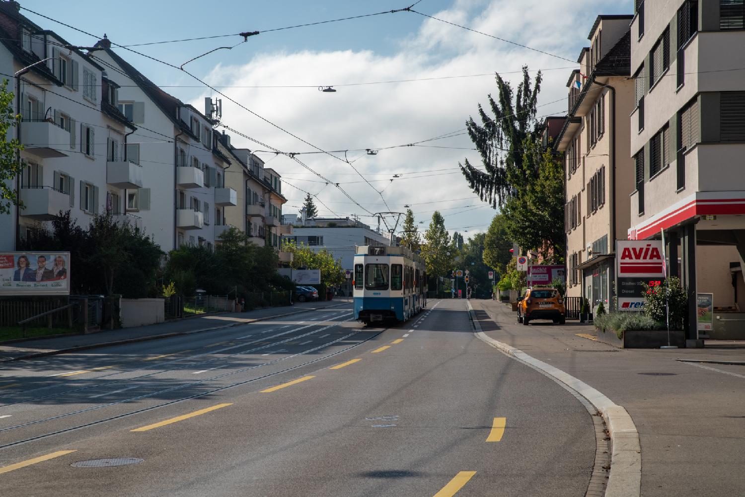 A street with 4-5-storey buildings on each side, an Avia petrol station, and a tram number 7 in the middle of the street