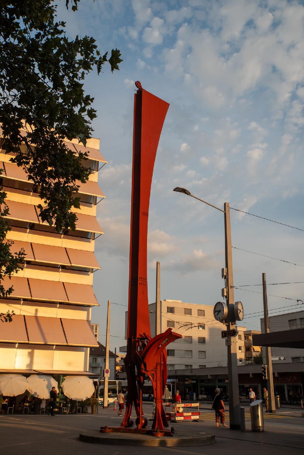 IBM-Stengel, a sculpture by Bernhard Luginbühl on Altstetterplatz in Zürich. This is a red, metallic, elongated sculpture.