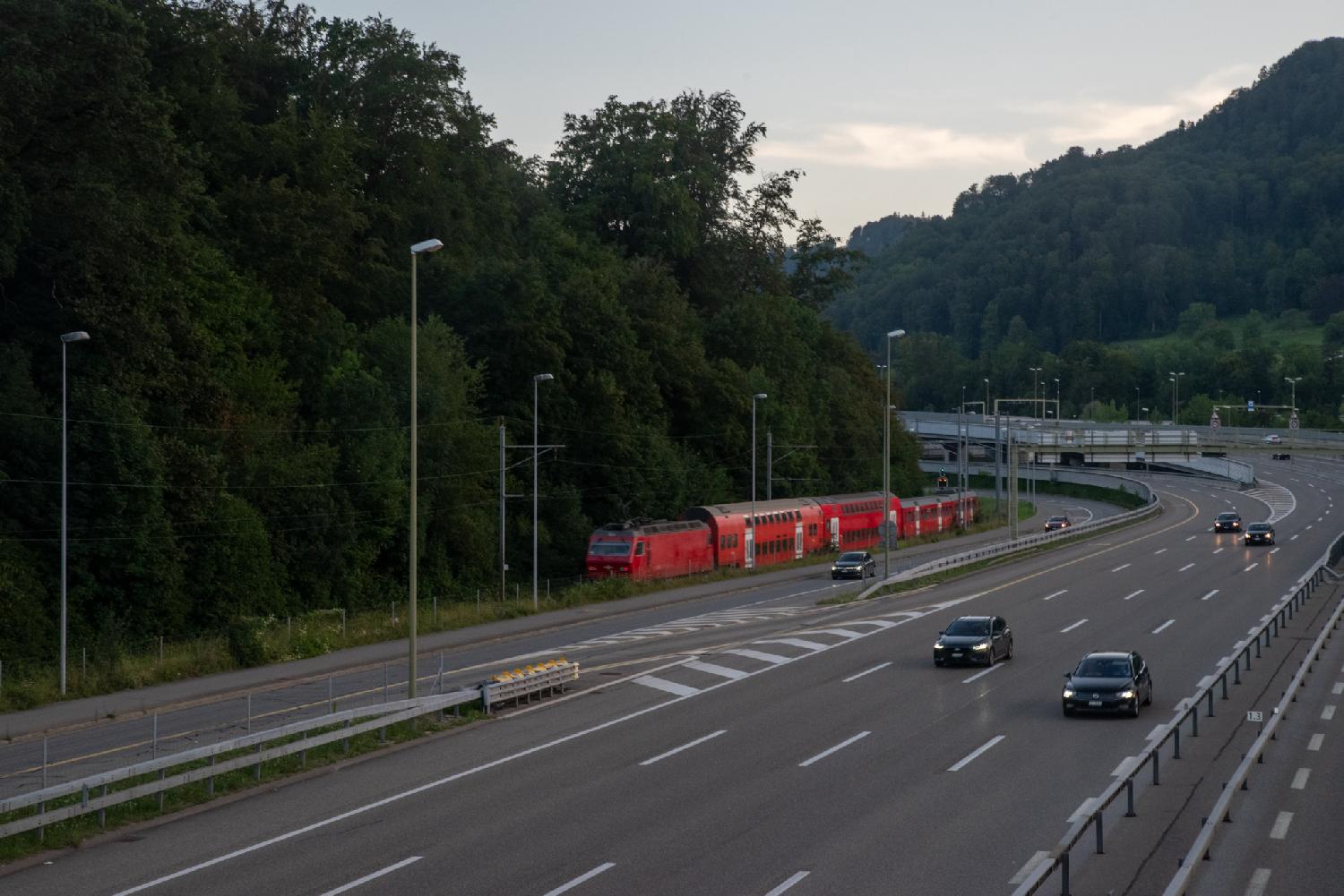 View from a bridge over a rail track, where a red train is running, and a highway.