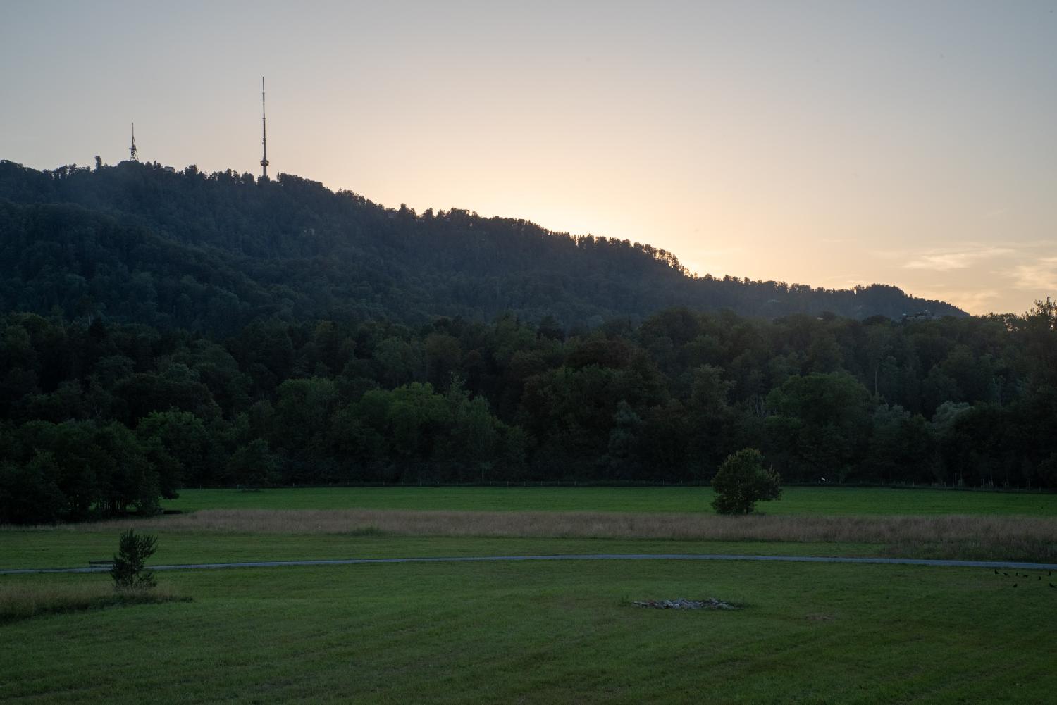 A large green grass area, with the Uetliberg in the background. The sun is setting behind the mountain.