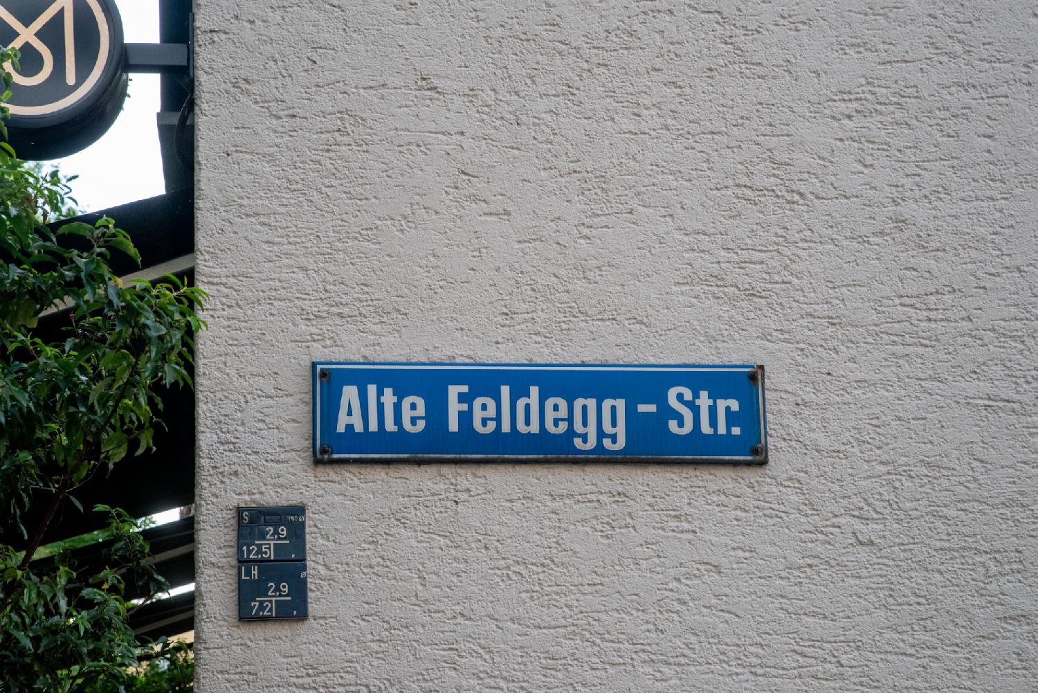 Zürich Alte Feldeggstrasse street sign: a blue sign on a beige textured wall