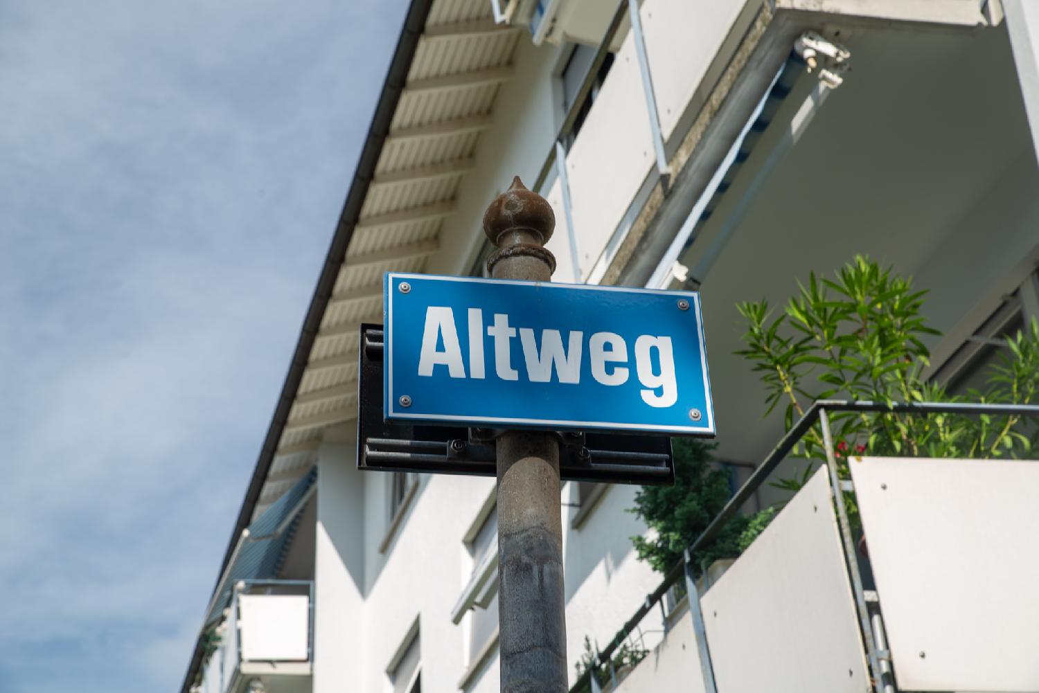 Zürich Altweg street sign: a blue sign on a metallic pole with a residential building with balconies in the background