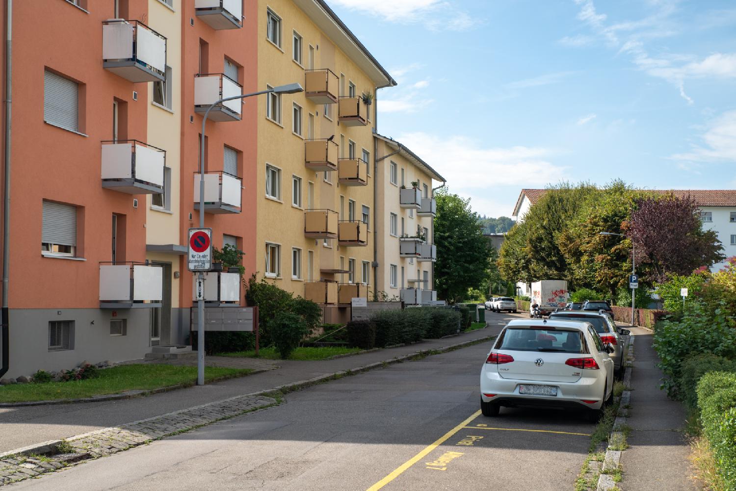 Altweg in Zürich: a road with parking spots on the right and 3-4-story buildings (coral, yellow, off-white) on the left.