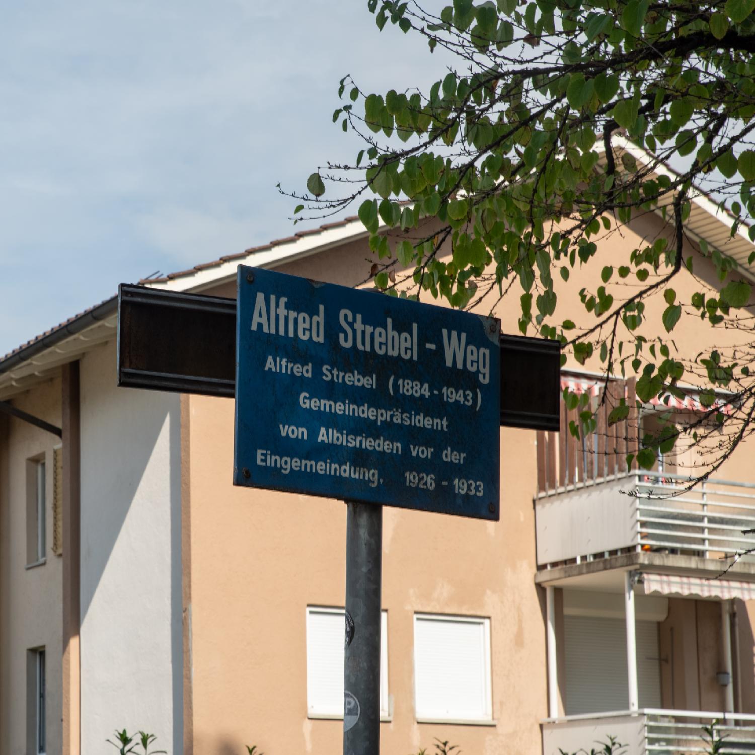 Alfred Strebel Weg street sign. The sign reads "Alfred Strebel (1884-1943) - Gemeindepräsident von Albisrieden vor den Eingemeindung (1926-1933)".