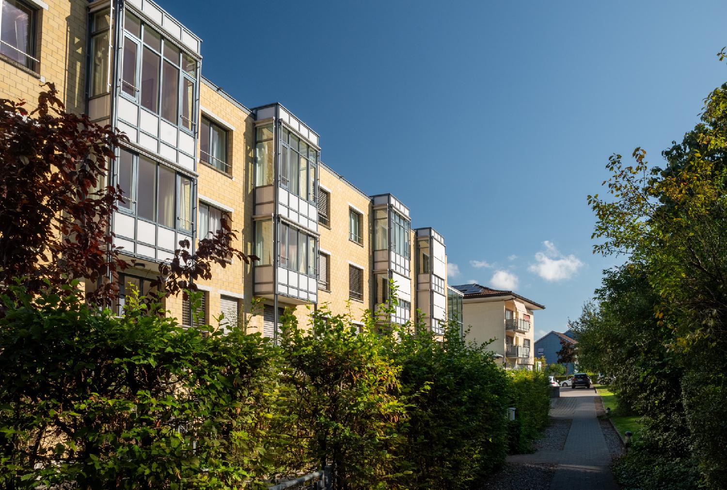 Alte Kalchbühlstrasse in Zürich: a narrow street with three-story buildings on its left. The buildings are brick-yellow and have windowed balconies protruding from the façade.