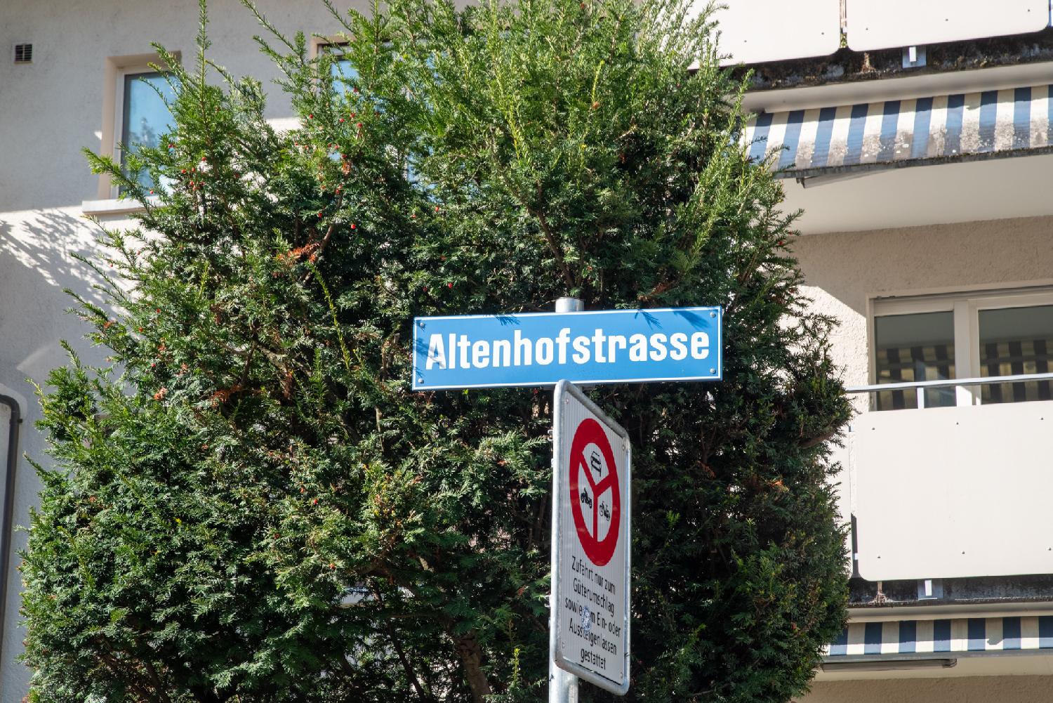 Altenhofstrasse street sign in Zürich: A blue sign in front of a tree and a residential building, with a "forbidden to all vehicules" signs below it