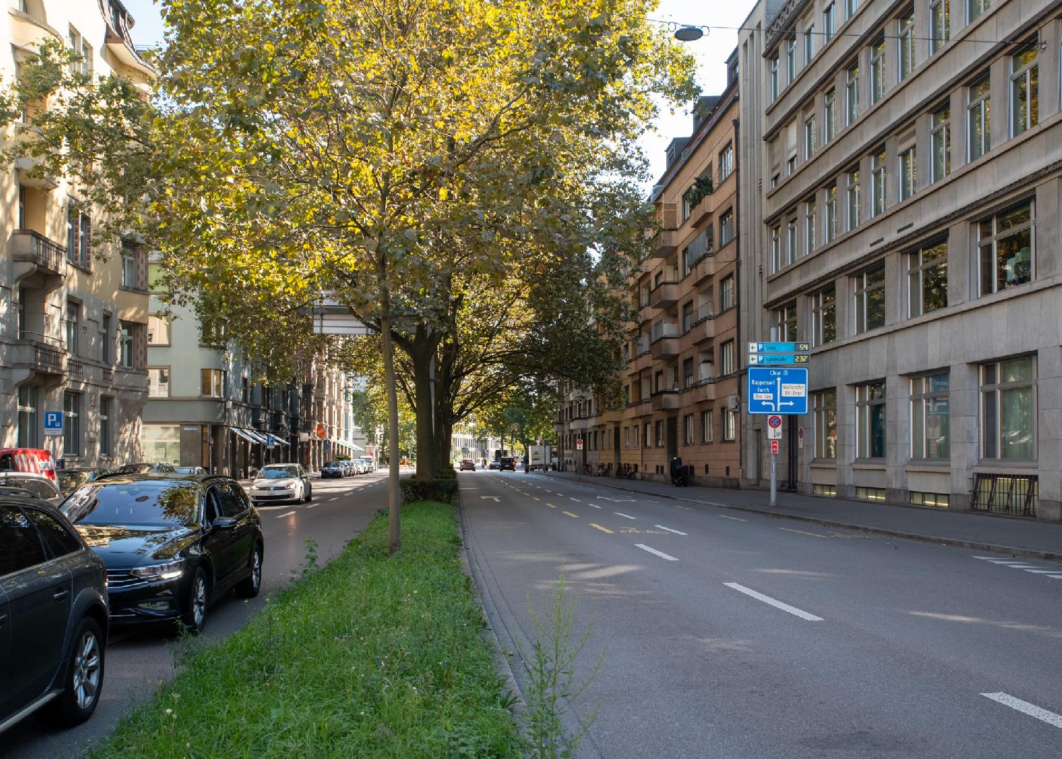 Zürich Alfred-Escher-Strasse - a two-way, four-lane street split by an island with plane trees. There are 5-6-story buildings on each side of the street.