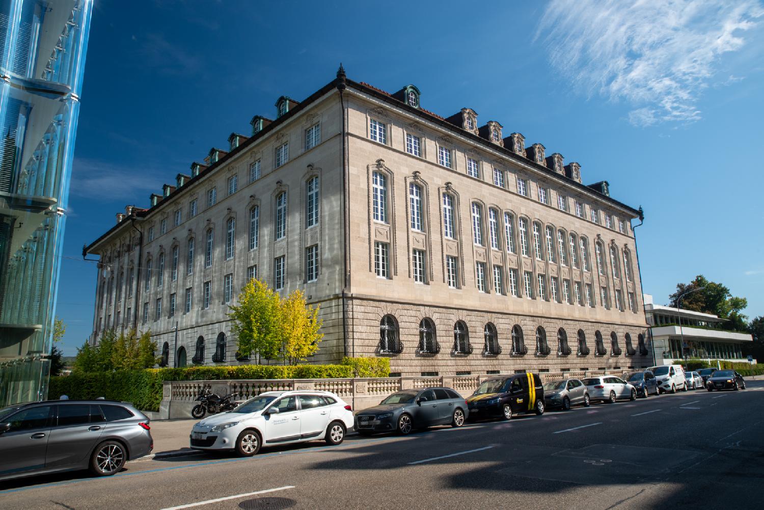 A stone building with high windows; another more modern glass building is visible on the left side.