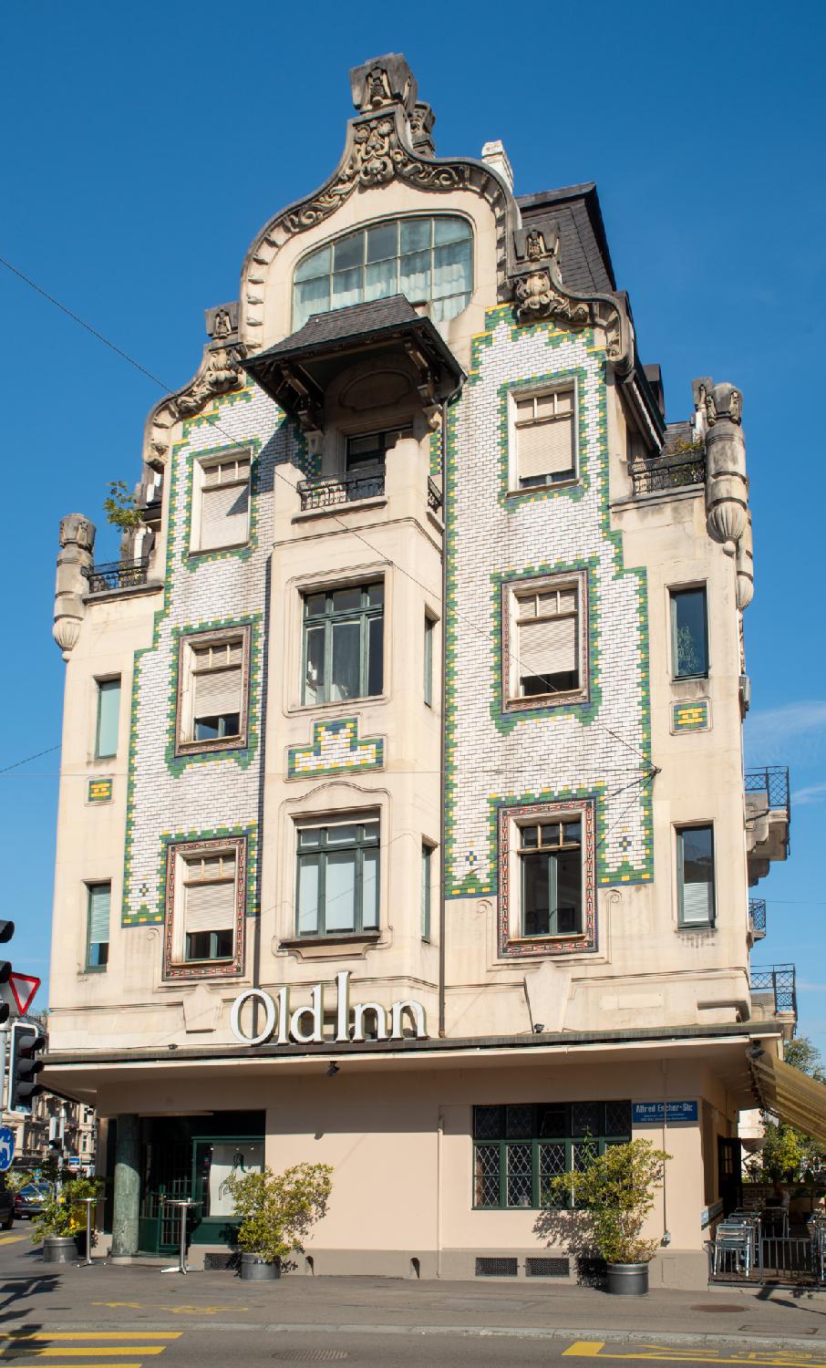 A building with a curvy top and white and green tiles on the facade, and an Old Inn sign above the ground floor.
