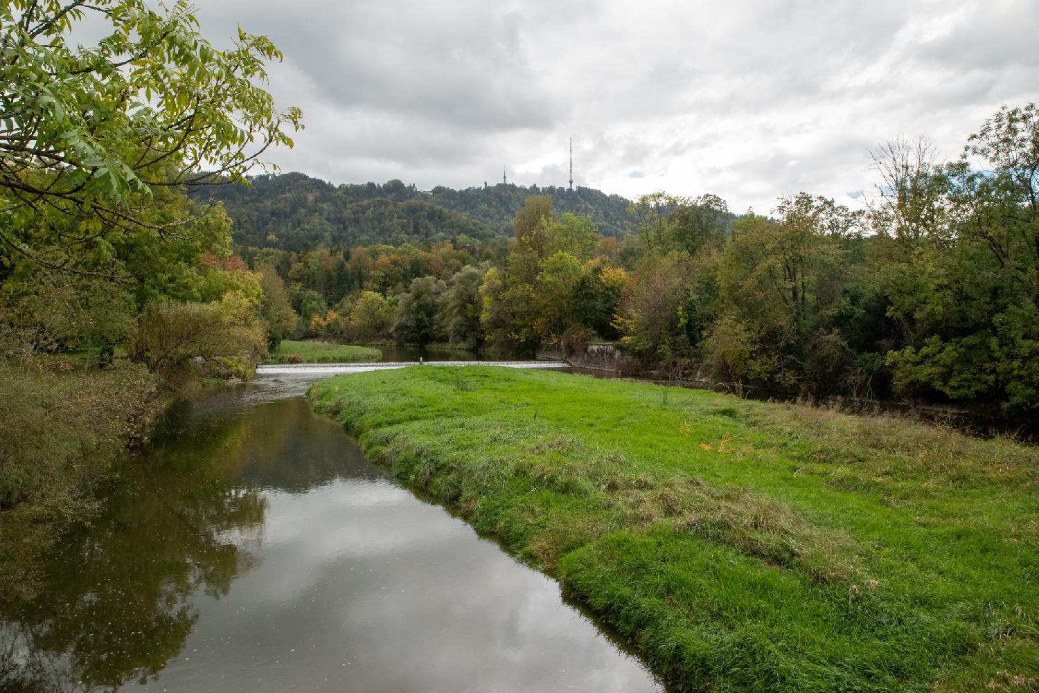 View on the Sihl and the Uetliberg from Allmendbrücke in Zürich: a quiet river with a hill in the background and a meadow on the right side