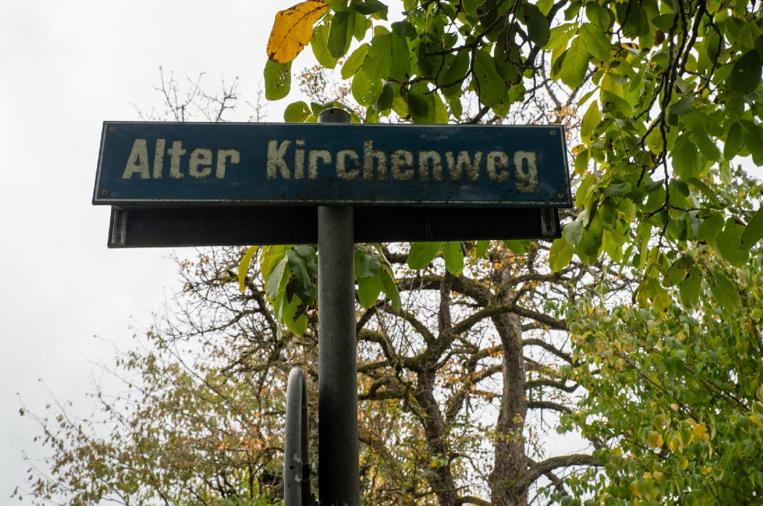Zürich Alter Kirchenweg street sign: a blue sign, somewhat dirty, in front of tree leaves