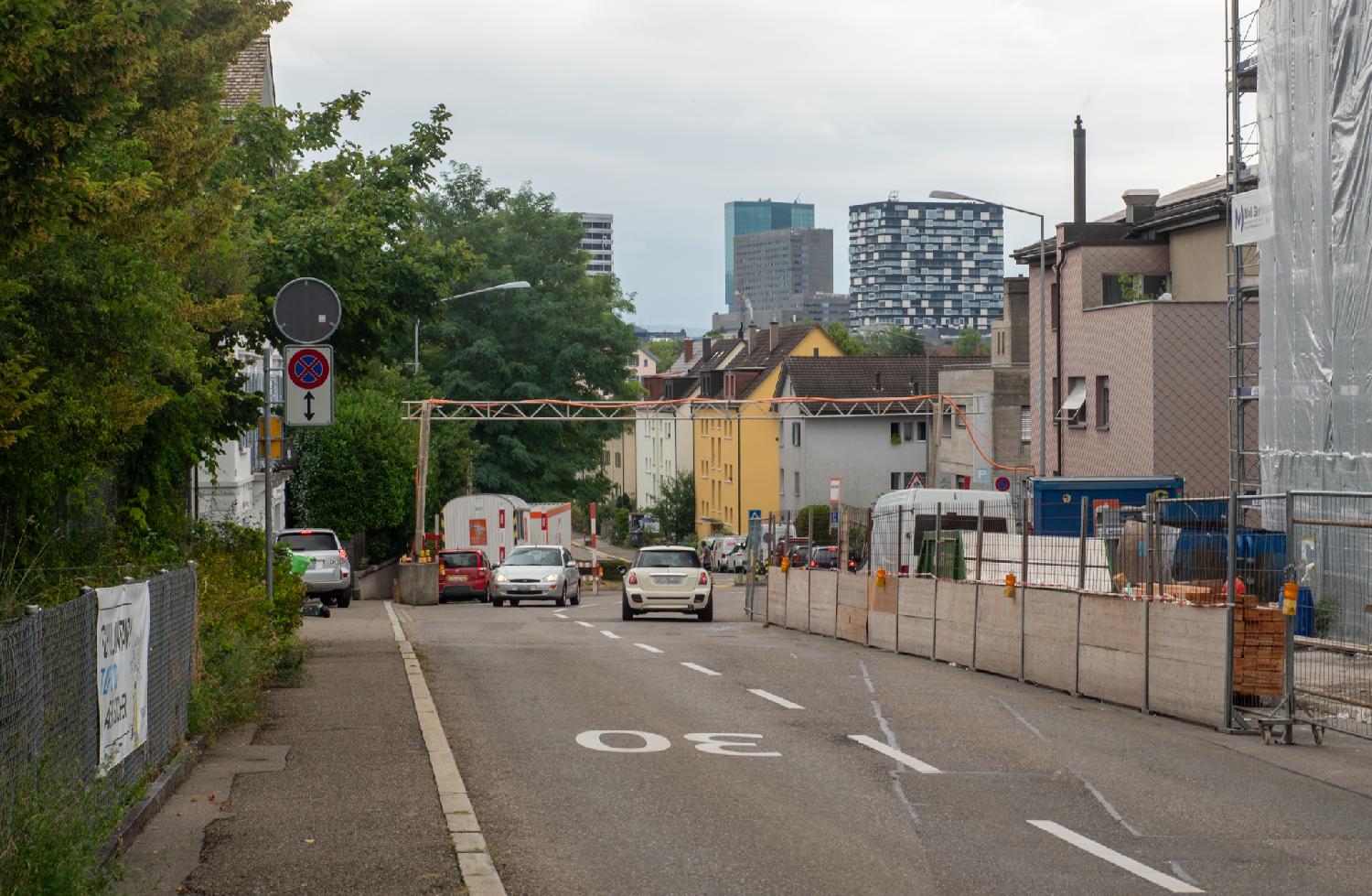 A two-way street with a car in each direction, building construction works on the right and high-rise-buildings in the background.