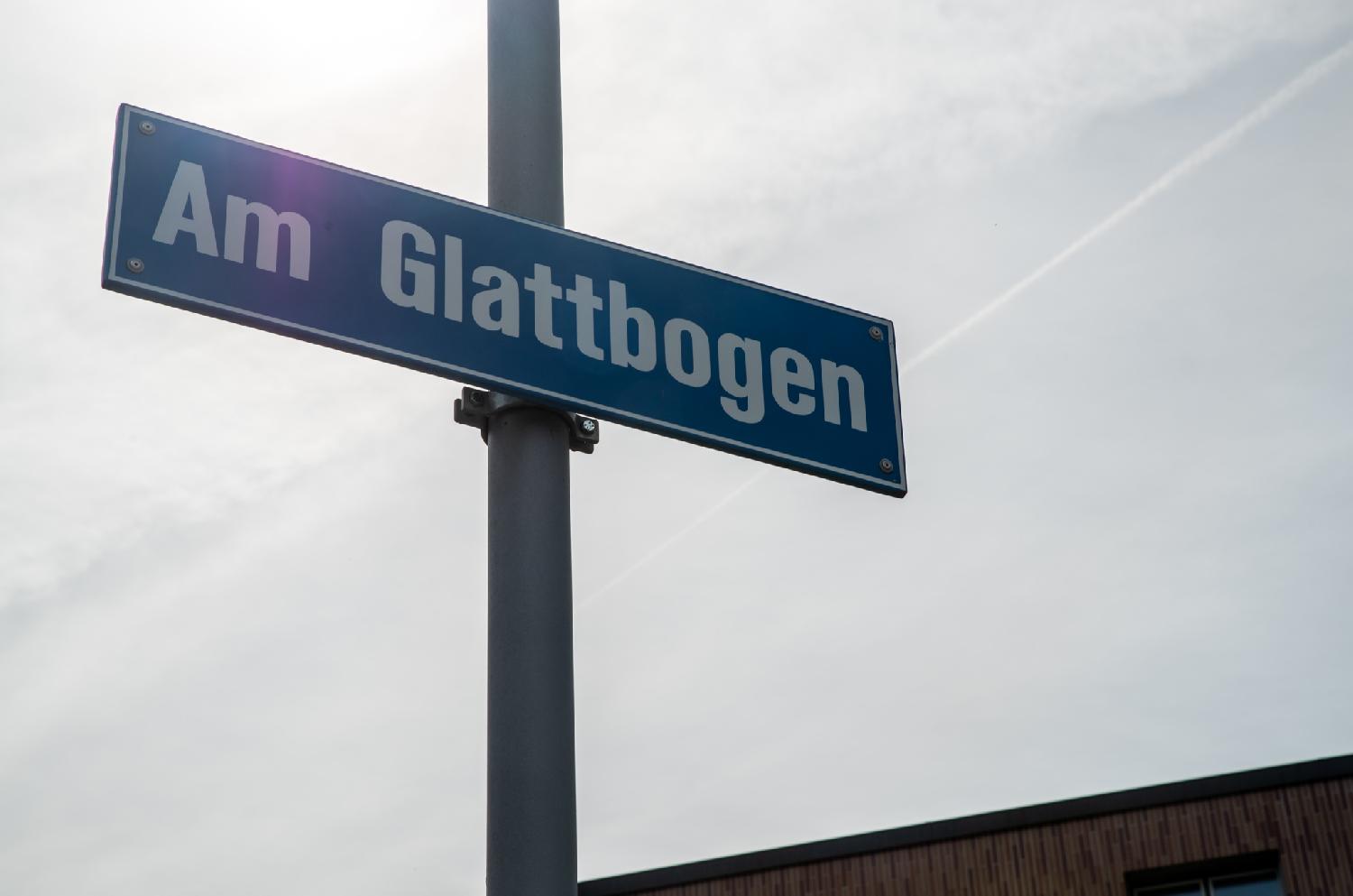 Street sign of Am Glattbogen in Zürich: a blue sign on a metallic pole, in front of cloudy grey sky.