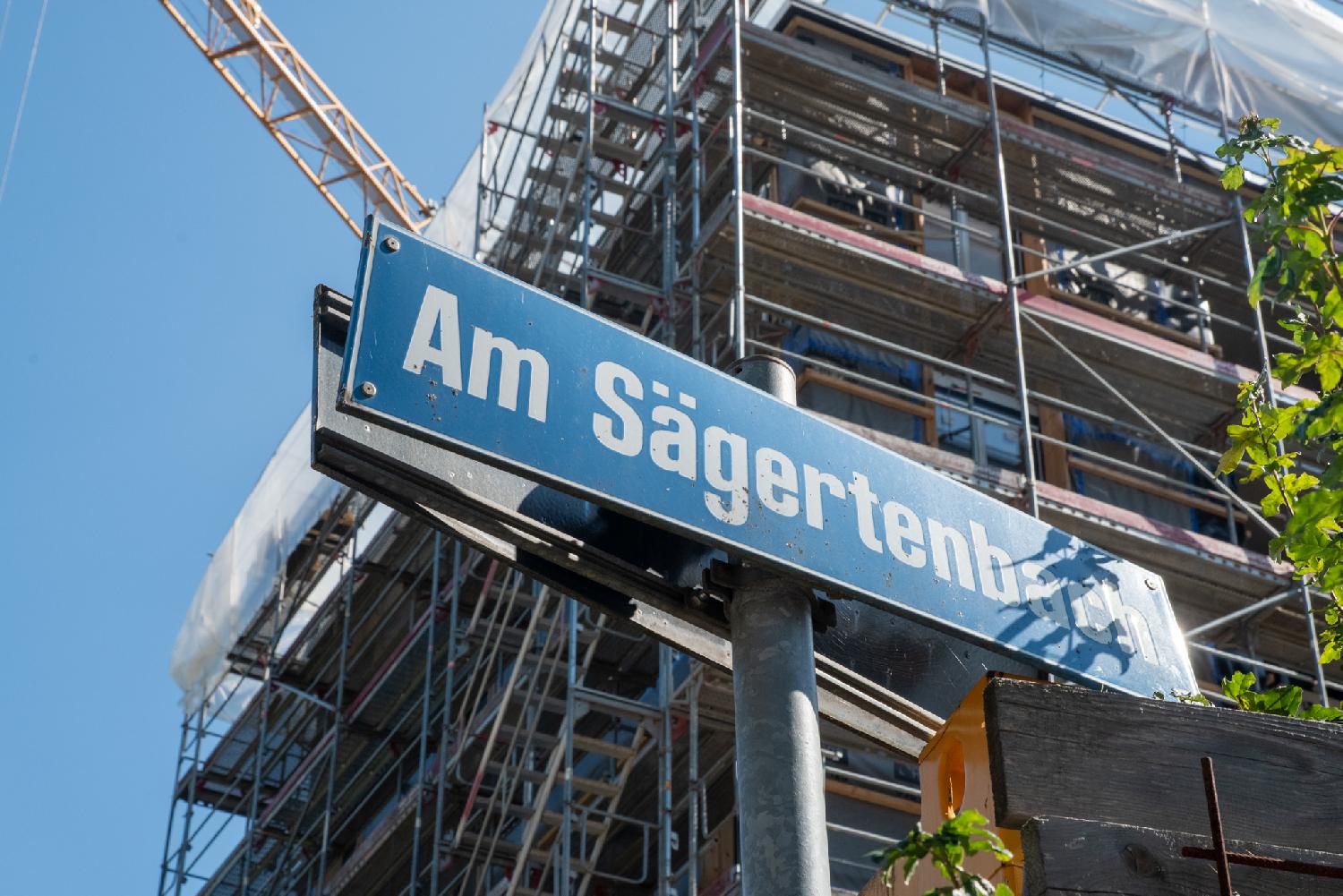 A blue "Am Sägertenbach" street sign in front of a building still in construction