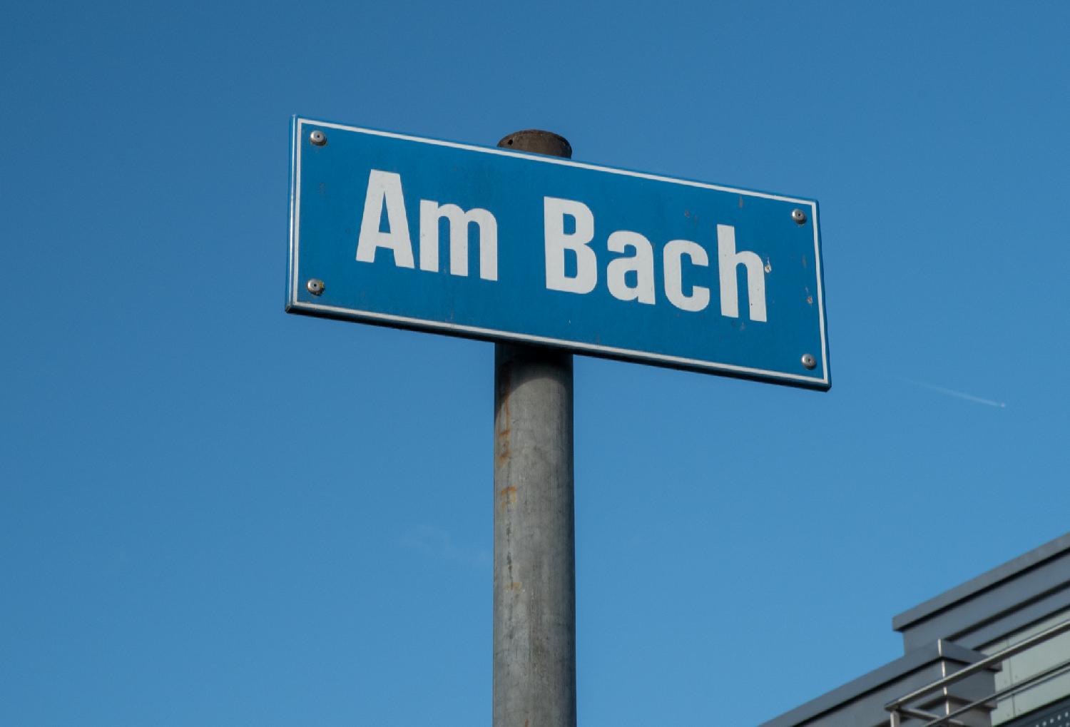 Street sign of Am Bach in Zürich: a blue sign on a metallic pole in front of a blue sky
