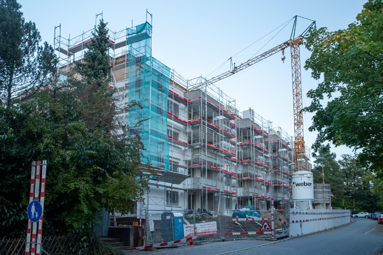 A construction site for a 4-story building with scaffolding and a crane in front of it.