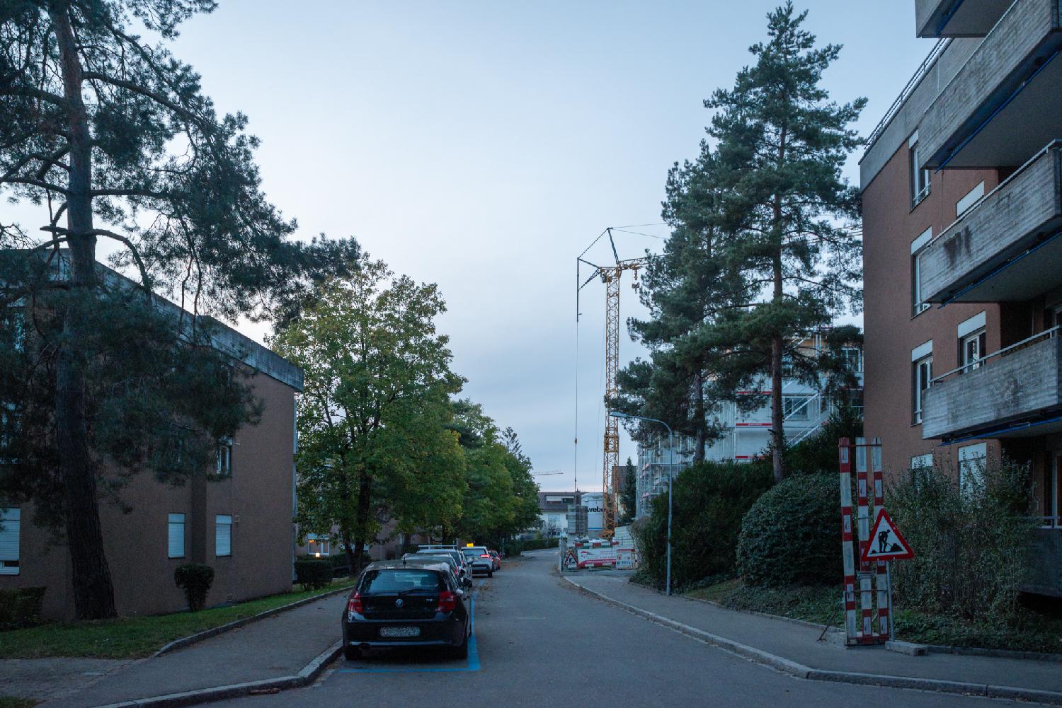 Am Holbrig in Zürich: a residential street with cars parked on the left, 3-4-story buildings, and a crane in the background in front of a construction site.