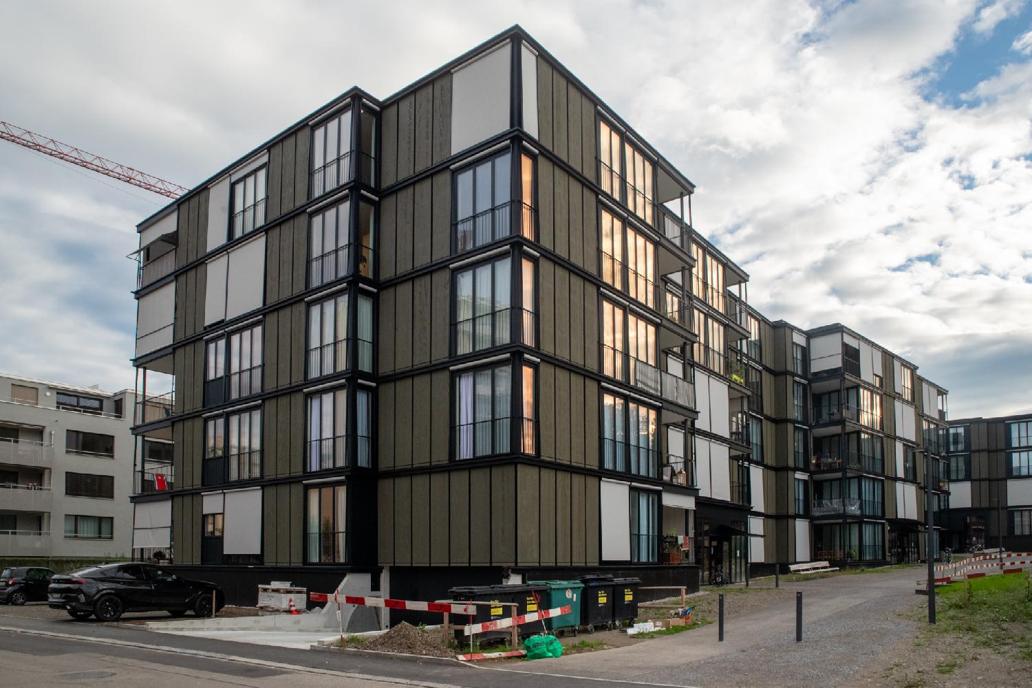 A 5-story set of brown and glass buildings. The buildings are new, there is still some building equipment lying around.
