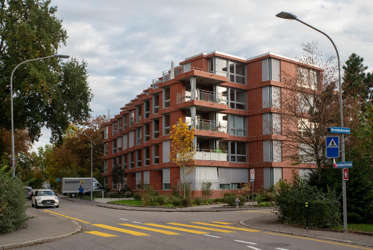Altwiesenstrasse in Zürich: a two-way street with a yellow zebra, at an intersection, with a brick red 4-story building aligned in a stair line.
