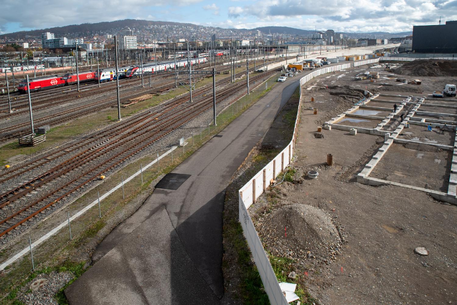 A street, seen from above, with railway tracks on the left and construction work (with white palisade) on the right. The street doesn't look accessible to the public.