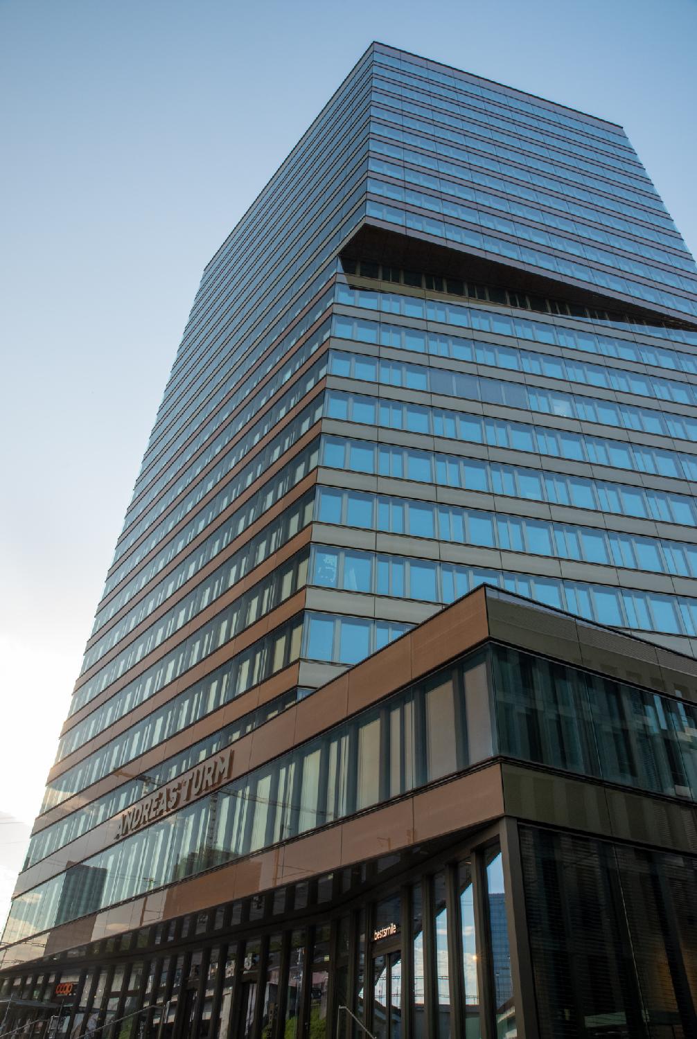A high-rise glass-paned building with brown stripes, seen from the ground. The words Andreas Turm are written on the facade.
