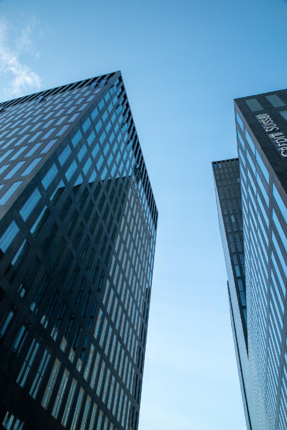 Two glass high rise buildings in front of each other, the right one reflecting on the left one. The right one has a Crédit Suisse logo.
