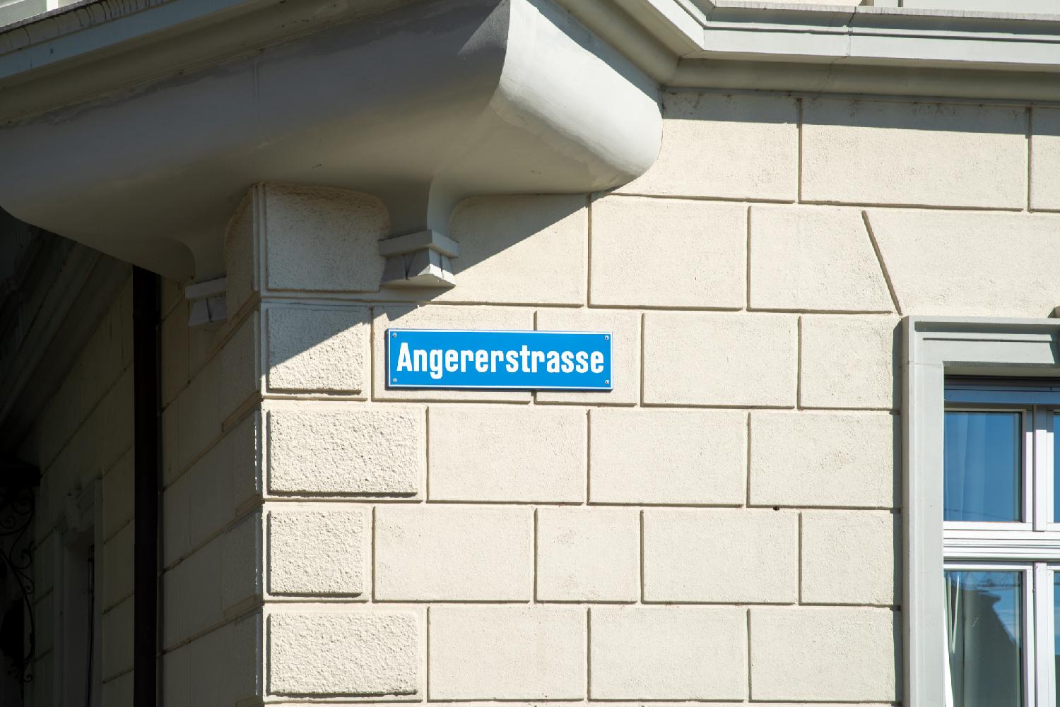 A blue "Angererstrasse" street sign on a white stone wall.