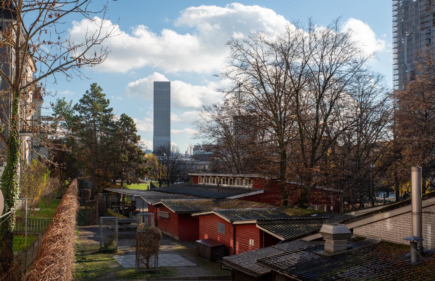 A high windowless tower in the background, standing out against blue sky, with small red buildings in the foreground.