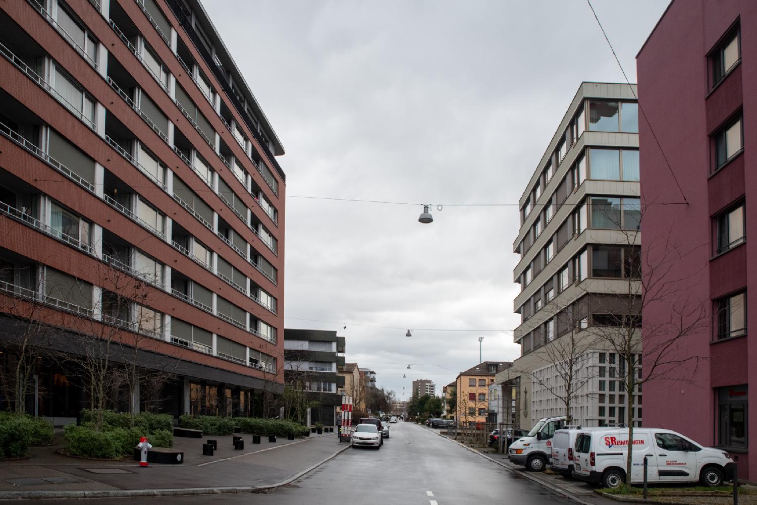 A two-way street with cars parked on each side and 4-to-10-story building on each side.