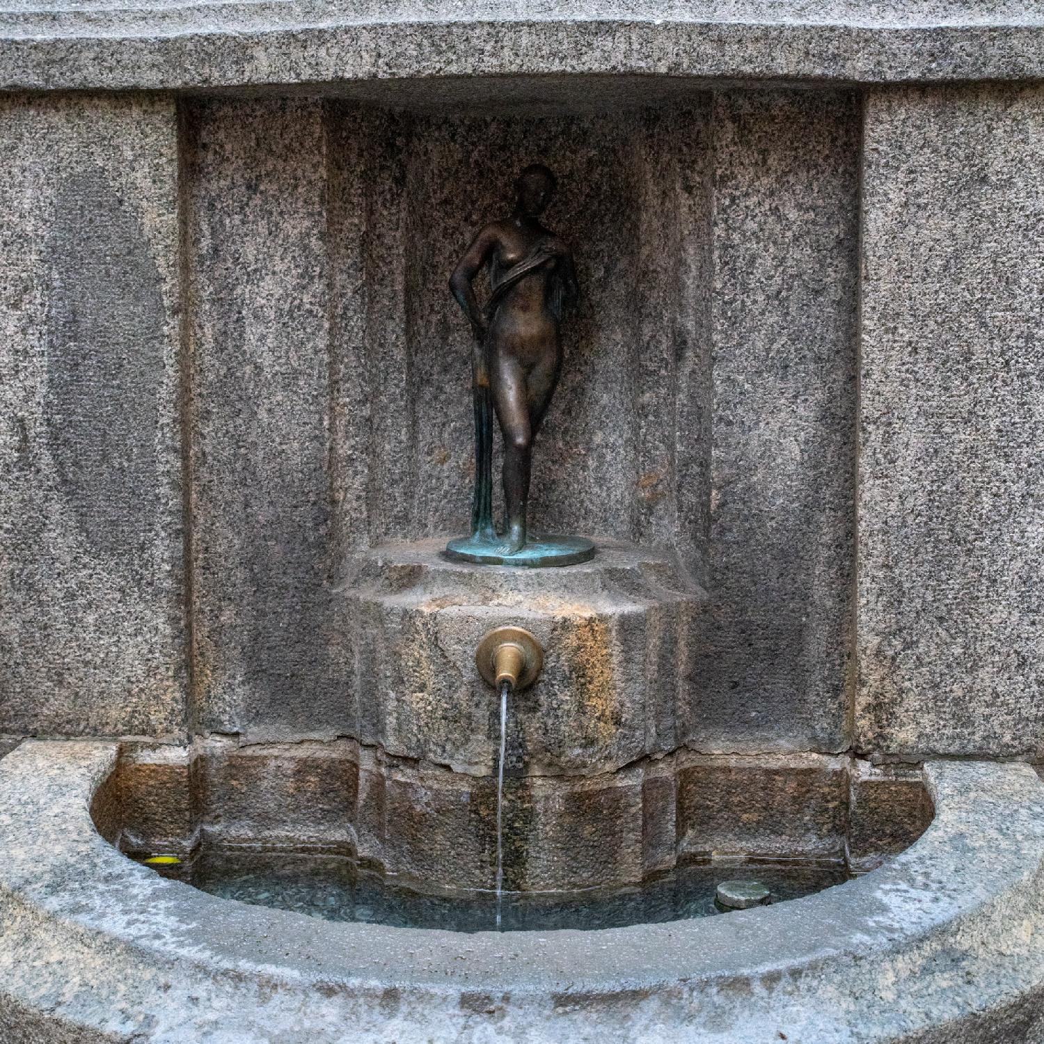 A hanging sign with a man wearing suspenders decorated with cows and smoking the pipe, a small Swiss flag, and decorative golden frame, with Aelpli Bar written below it.
