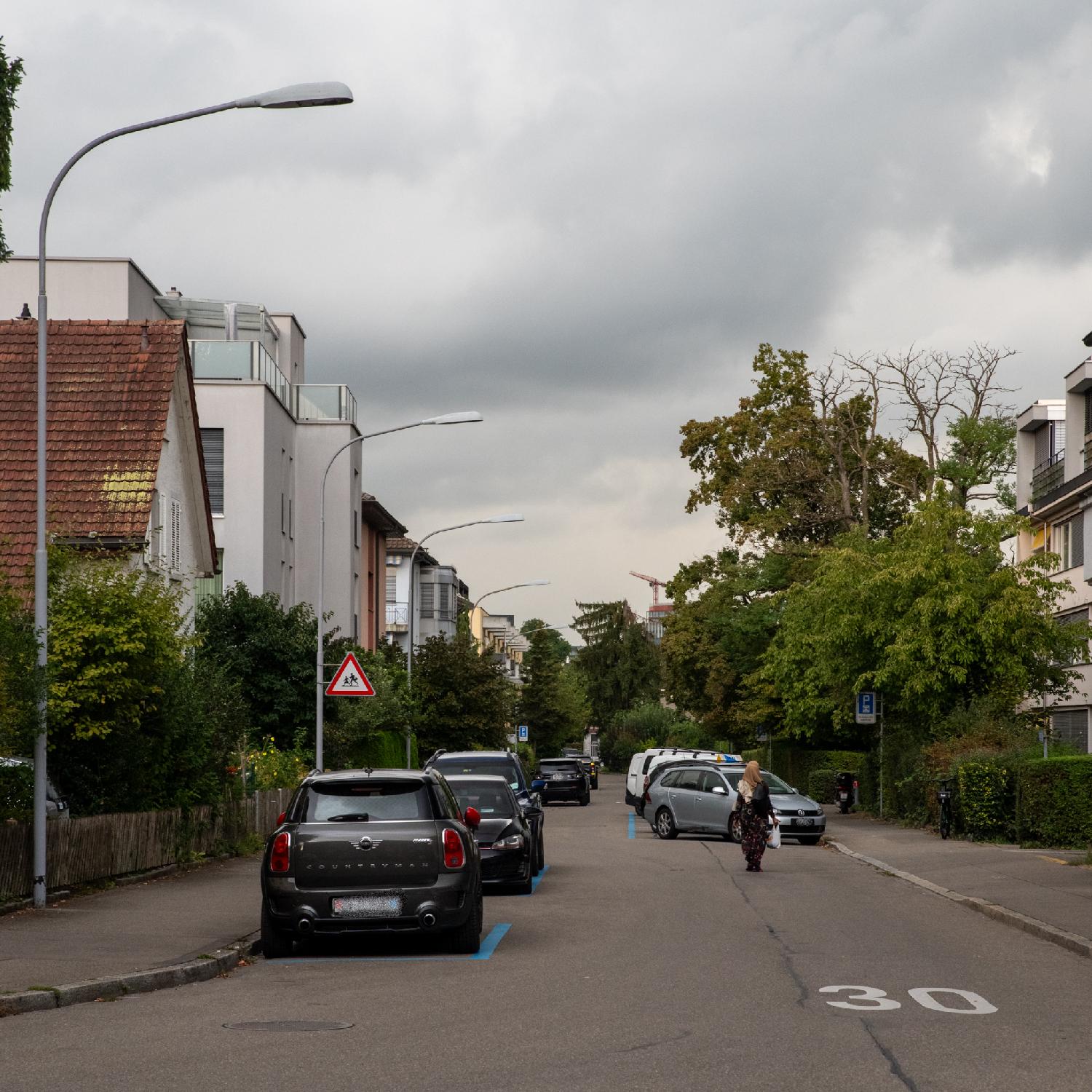 A residential street with 2-3-story buildings and cars parked on each side