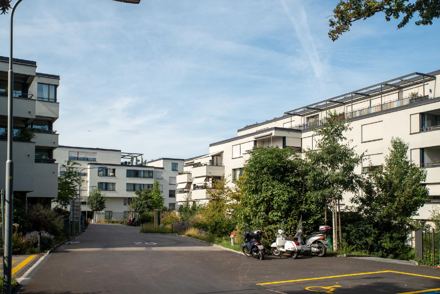 A residential area with 4-story white buildings all around a 20-km/h-limited street.