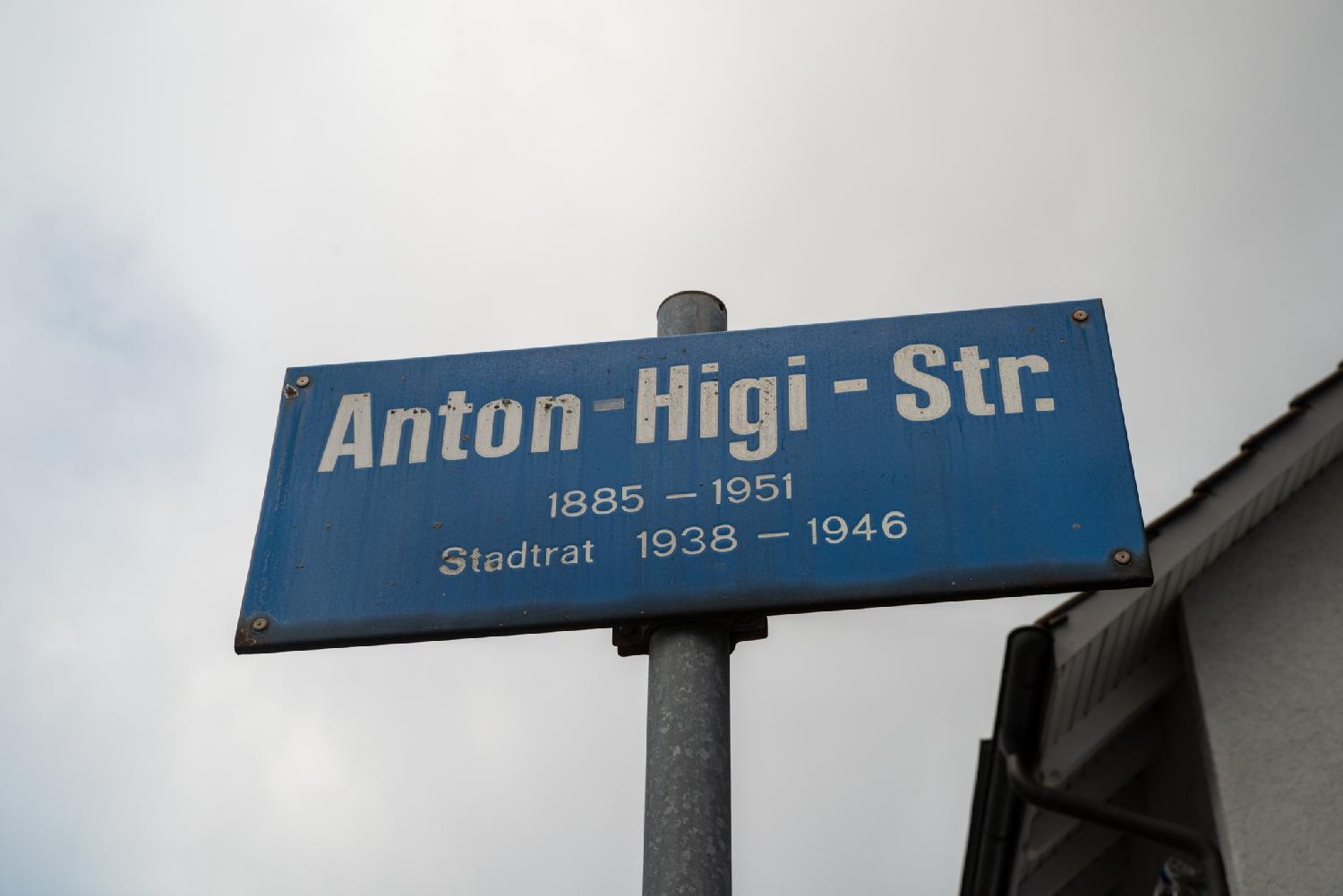 A blue street sign reading "Anton-Higi-Str. - 1885-1951 - Stadtrat 1838 - 1946"