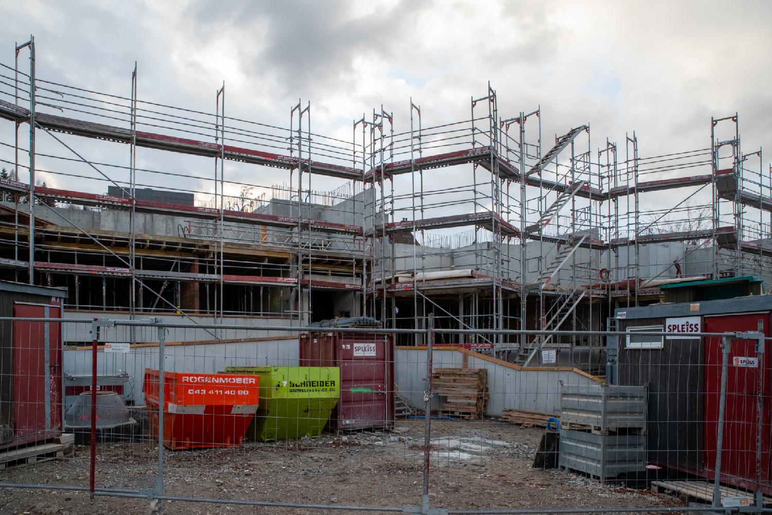 A construction site. The first floor has been raised; there is scaffolding that goes up another floor, and construction material dumpsters on the ground.