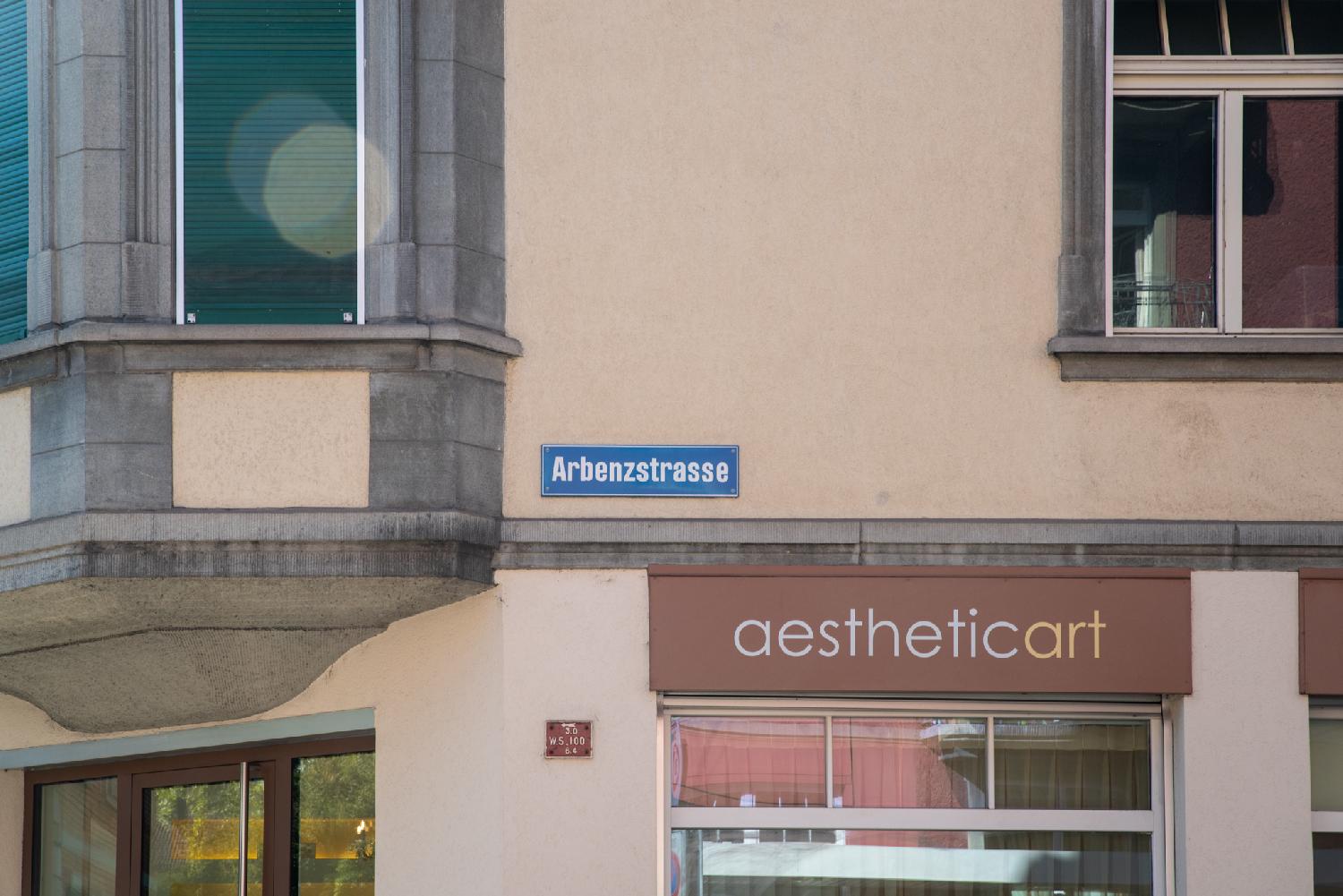 A building facade with parts of windows, a shop front, and a blue Arbenzstrasse street name sign attached to the wall.
