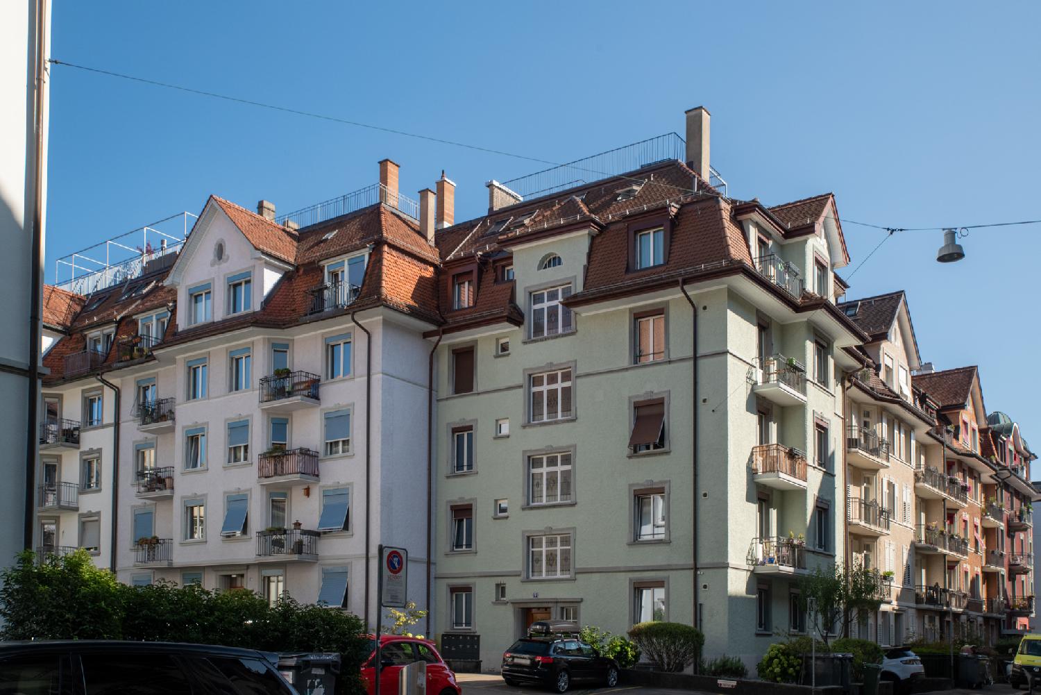 Corner of a street with 5-story residential buildings with tiled roofs and dormer windows.