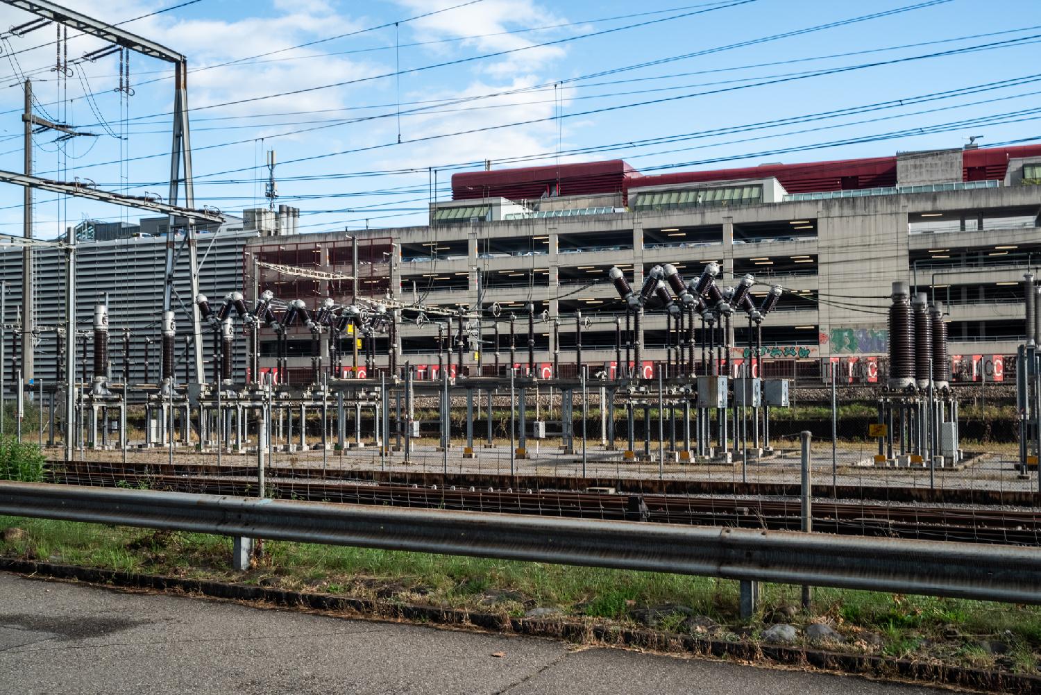 An electrical substation in front of a multi-story parking lot.