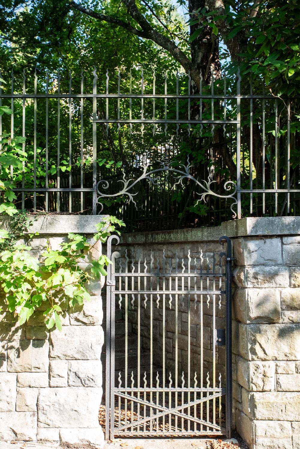 A metallic gate to an area with trees between two stone walls