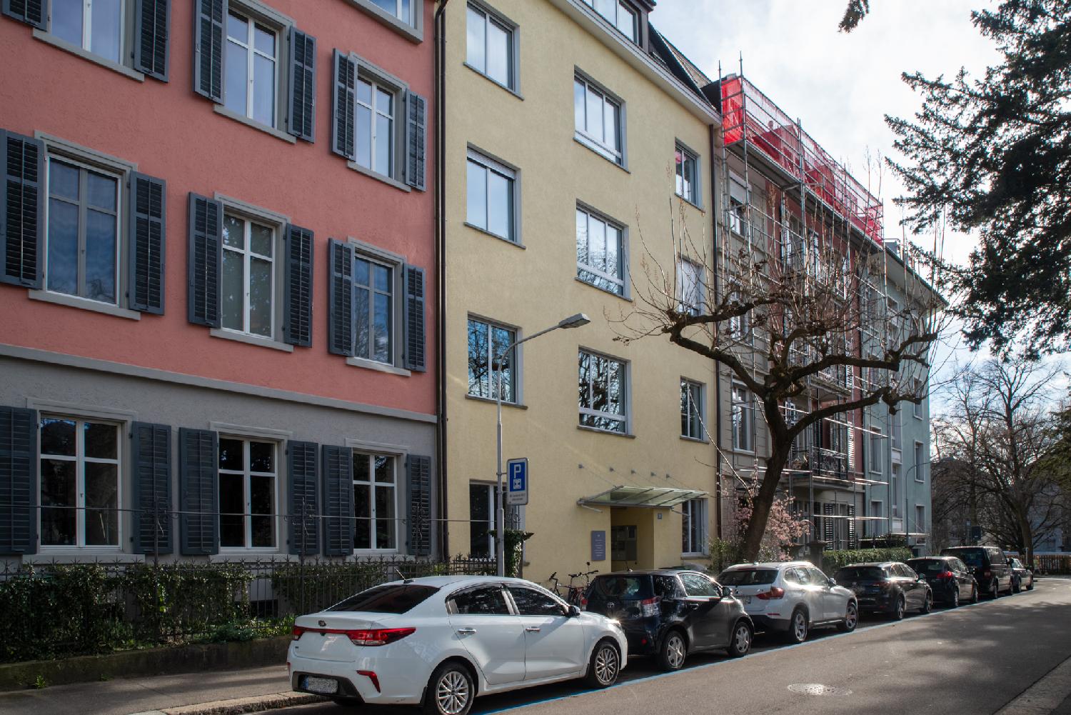 Colored facades of 4-story residential buildings on a street with cars parked in front of them