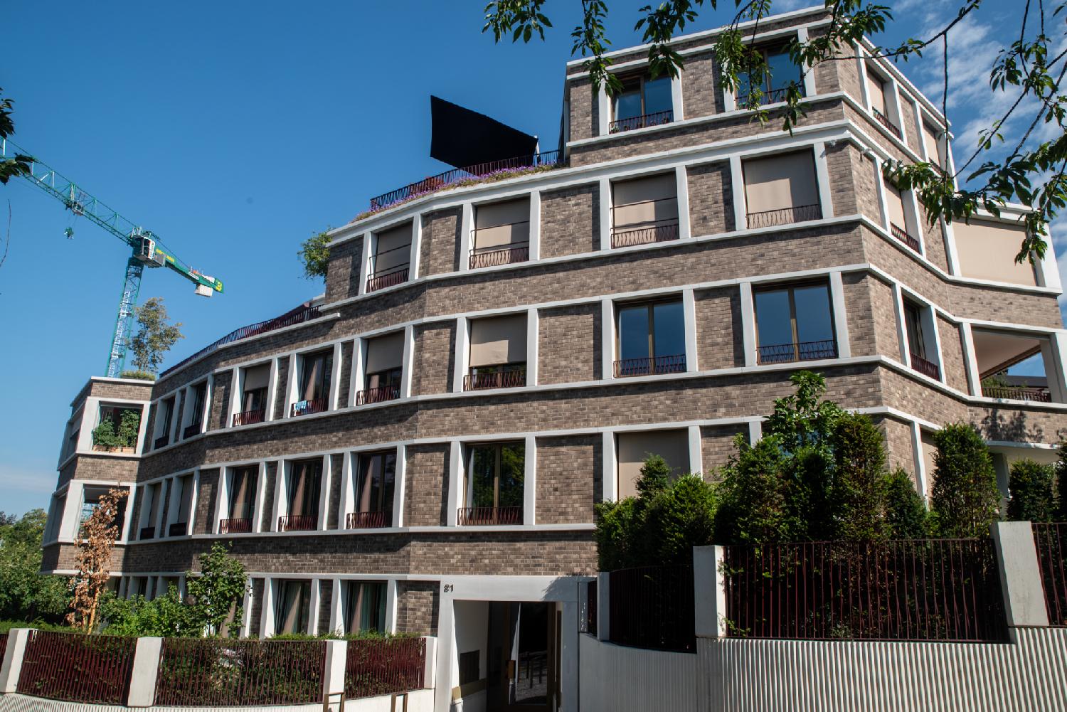 A 5-storey residential building in brown bricks and white frames, with the fourth and fifth floors receding to yield space for rooftop terraces